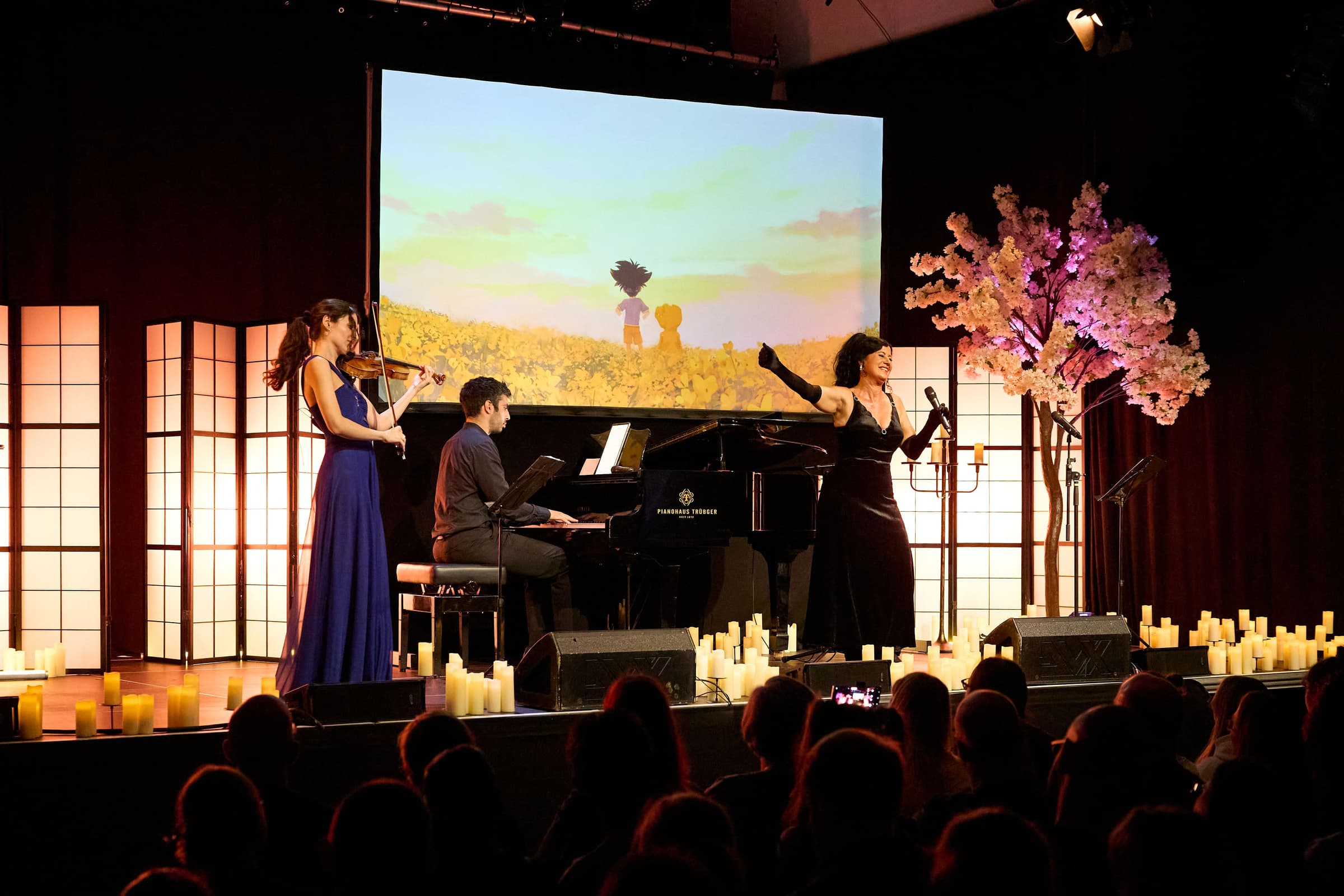 Bühne des Anime Legends Concert mit Flügel, Kirschblütenbaum und Projektion, davor das Publikum