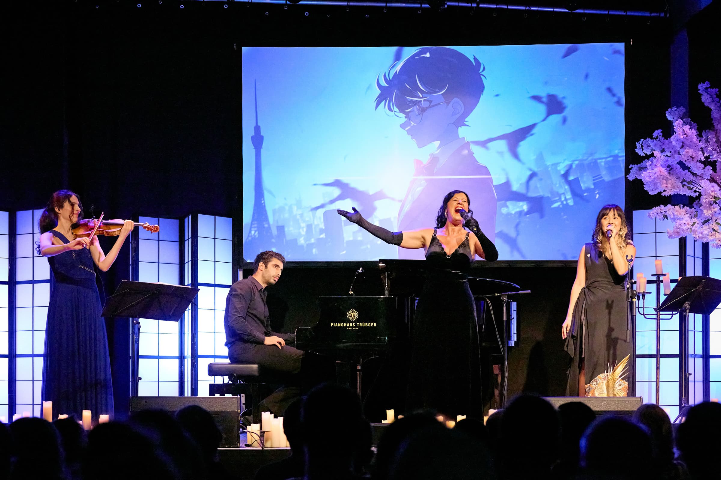 Violinistin, Pianist und Sängerin auf der Bühne vor einer Anime-Projektion