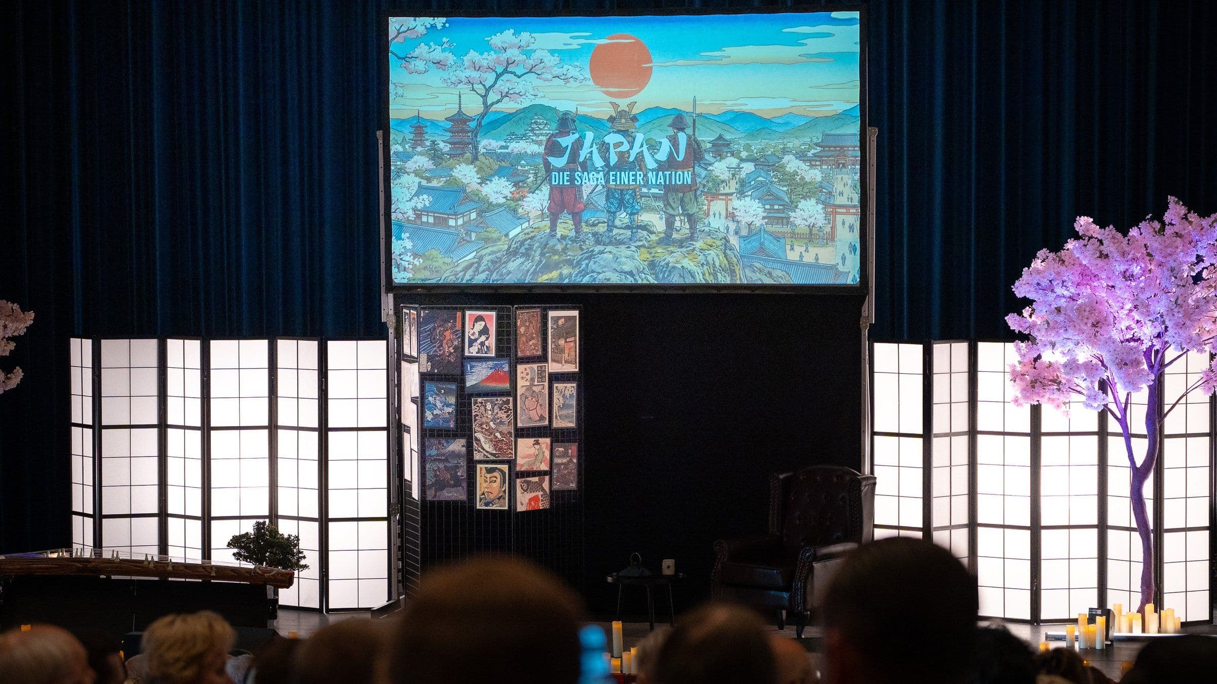 Blick aus dem Publikum auf die Bühne von „Japan – Die Saga einer Nation“ mit Projektion, Shoji-Wänden und Kirschbaum
